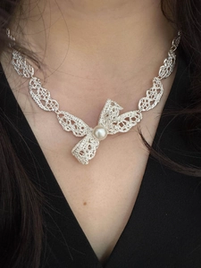 Gros plan d'un collier pendentif nœud perlé avec texture dentelle porté au cou