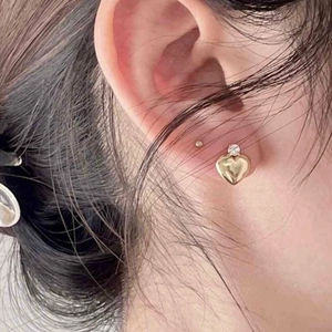 Close-up of heart-shaped gold stud earring with zircon stone on woman's earlobe