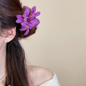 Close-up of purple fabric flower hair pin styled on a brunette bun with pearl jewelry