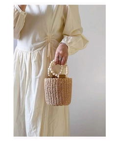 Detail of hand-woven straw bucket bag featuring large cream beaded handles and natural texture