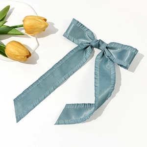 Detail of blue satin bow hair clip with ruffle edges and silk texture on white surface