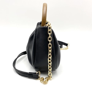 Detail of black pleated cloud bag with natural wood handle and gold chain strap