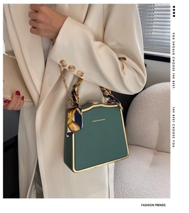 Detail of green box bag with gold metal trim and decorative floral silk scarf on handle