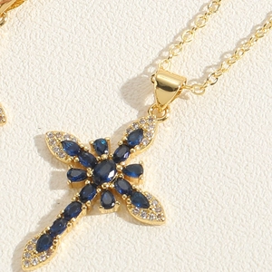 Macro shot of gold cross pendant necklace featuring a blue gemstone and pavé diamonds