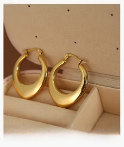 Detailed macro view of gold-plated U-shaped chunky hoop earrings on beige velvet