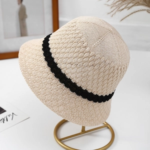 Detailed macro view of a beige knitted bucket hat with a black stripe on a stand.