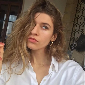 Detail of 18k gold letter A necklace and hoop earrings worn by a model in natural light