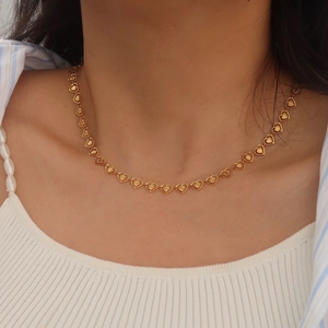 Close-up of gold heart-shaped choker necklace with sunburst texture on model's neck