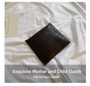 Detail shot of a black crocodile-embossed zip pouch on a white fabric background