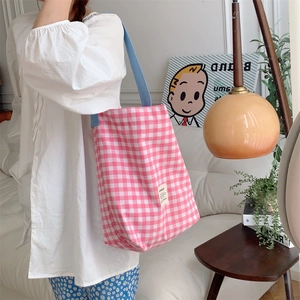 Sac fourre-tout en toile à carreaux roses avec anses bleues porté à l'épaule par un mannequin