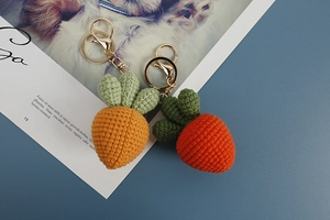 Macro shot of two handmade crochet carrot keychains with gold metal lobster clasps