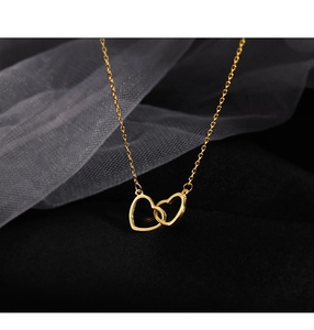 Detail of interlocking golden double heart pendant necklace on a soft mesh background