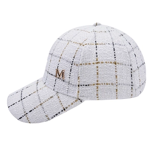 Detail of white tweed baseball cap with gold metallic M logo and plaid pattern texture