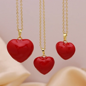 Three gold necklaces with red heart pendants hanging over elegant pink satin fabric