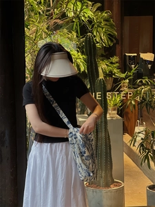 Blue and white floral crossbody bag with hat styled in a natural outdoor cafe setting