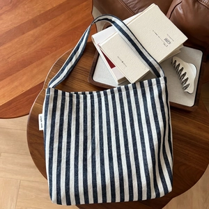 Detail of blue striped canvas tote bag with a white woven simple wish side label