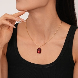 Close-up of a vintage dark red rectangular pendant necklace on a gold chain worn by a model