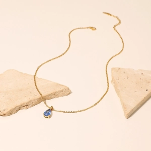 Detailed view of an 18K gold plated chain with a pear-shaped blue zircon pendant on stone