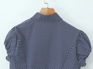 Rear view of a navy blue polka dot blouse with puff sleeves and button-up detail