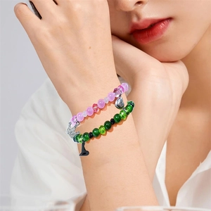 Close-up of pink and green beaded friendship bracelets with crown and heart charms on wrist