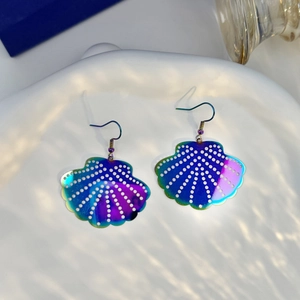 Close-up of iridescent shell earrings with white dots on a wave-textured ceramic tray