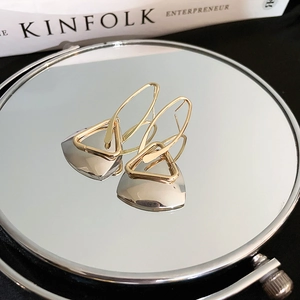 Macro detail of gold geometric triangle earrings resting on a mirror with magazine