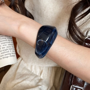 Close-up of a wide dark blue marble acrylic bangle with high-gloss finish on a woman