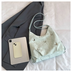Pale green pleated shoulder bag with metal butterfly accent shown next to an iPad for size