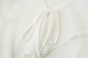 Detail of white knit shirt featuring V-neck lace-up bow and delicate ruffle edge trim