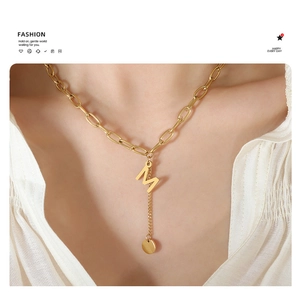 Detail of gold M initial pendant with round coin tassel on thick chain necklace