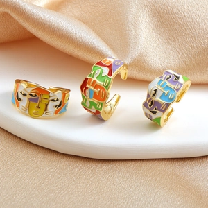 Three gold-plated adjustable enamel face rings set on a champagne silk background
