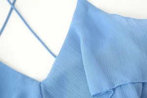 Detailed view of sky blue tiered dress featuring pleated fabric and thin spaghetti straps
