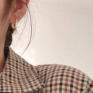 Detail view of minimalist gold curved stud earrings worn with a neutral plaid shirt