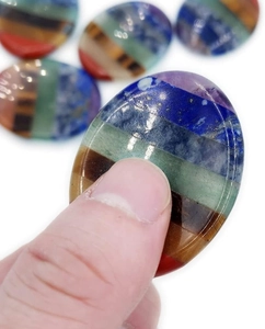 Macro detail of hand holding a polished seven-layer chakra thumb stone for relaxation