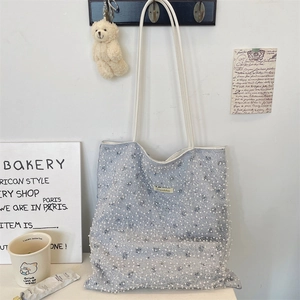 Detailed view of blue canvas tote with pearl mesh overlay hanging on a white wall