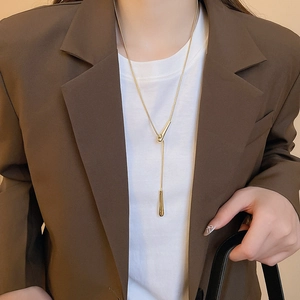 Detail of elegant gold teardrop pendant necklace worn with a stylish brown suit blazer