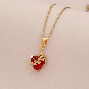 Gros plan du collier doré avec pendentif cœur rouge et détails de feuilles