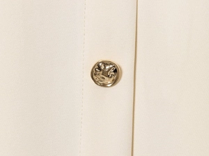 Détail macro d'un bouton métallique doré en relief sur le tissu beige d'un gilet