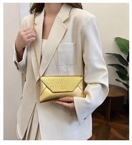 Détail d'une pochette enveloppe dorée à texture ondulée et élégante chaîne en métal doré