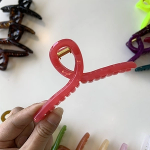 Detail of coral pink acrylic hair claw clip with golden spring on white surface