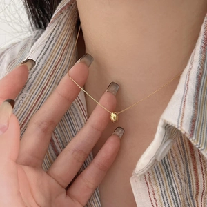 Detail view of a polished gold bean pendant necklace on a model with a striped shirt