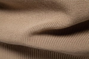Macro detail of khaki knit sweater fabric showing soft texture and ribbed hem craftsmanship