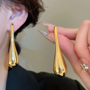 Close-up of golden teardrop pendant earrings with polished metallic mirror finish