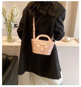 Detail of pink polka dot bucket bag with gold logo on black blazer outfit backdrop