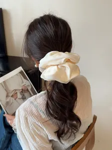 Detailed view of an elegant oversized cream satin scrunchie worn on a low ponytail hair style