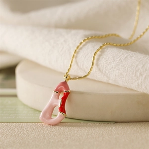 Vue macro du collier doré avec pendentif lettre en émail rose et rouge sur socle