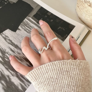 Macro shot of polished silver wavy ring showing minimalist fluid metal design on finger