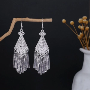 Detail of silver long tassel earrings with bohemian hollow patterns on wooden branch