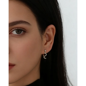 Detail view of a silver snake-shaped earring with crystals worn by a female model