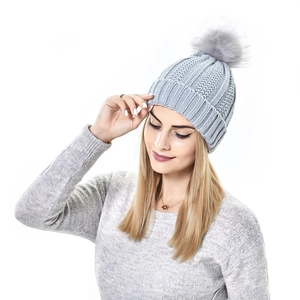 Close-up of light grey knit beanie with large faux fur pom-pom and thick cable pattern